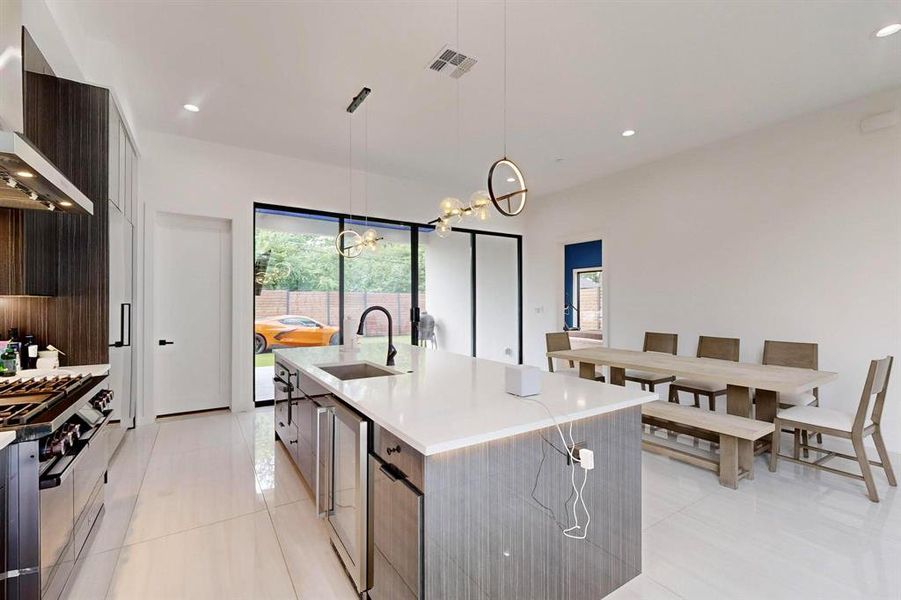 Kitchen featuring exhaust hood, modern cabinets, a chandelier, a center island with sink, and light countertops Kitchen featuring exhaust hood, modern cabinets, a chandelier, a center island with sink, and light countertops