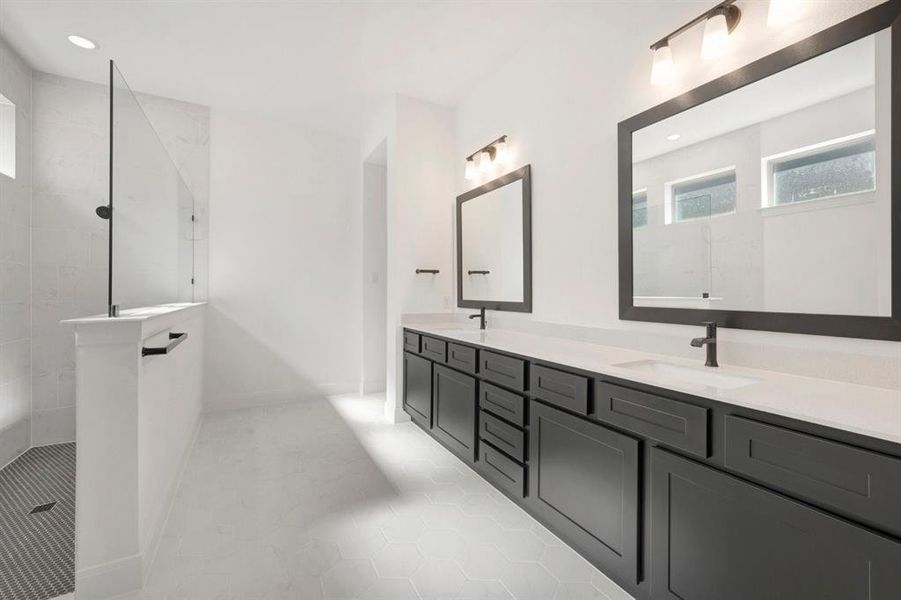 Contemporary bathroom featuring a spacious walk-in shower with a glass panel and dark-tiled floor, dual vanities with dark cabinetry and light countertops, two framed mirrors, and modern light fixtures Contemporary bathroom featuring a spacious walk-in shower with a glass panel and dark-tiled floor, dual vanities with dark cabinetry and light countertops, two framed mirrors, and modern light fixtures
