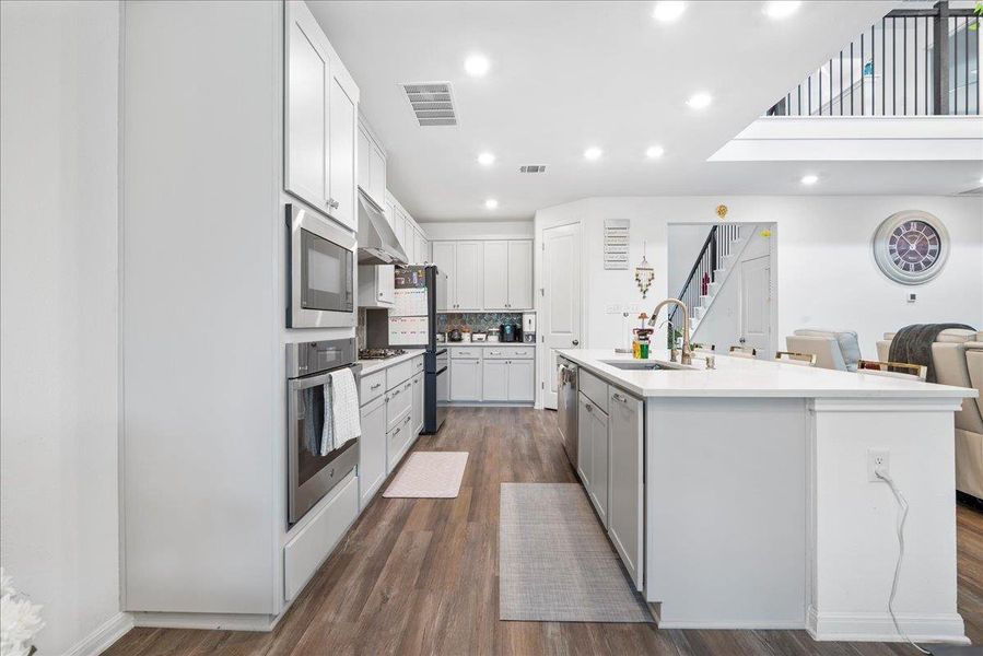 Kitchen featuring stainless steel appliances, an island with sink, dark wood-style flooring, recessed lighting, and white cabinetry