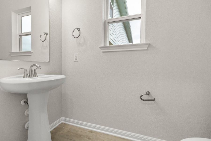 Bathroom featuring a white pedestal sink with a chrome faucet, a window providing natural light, and a mirror