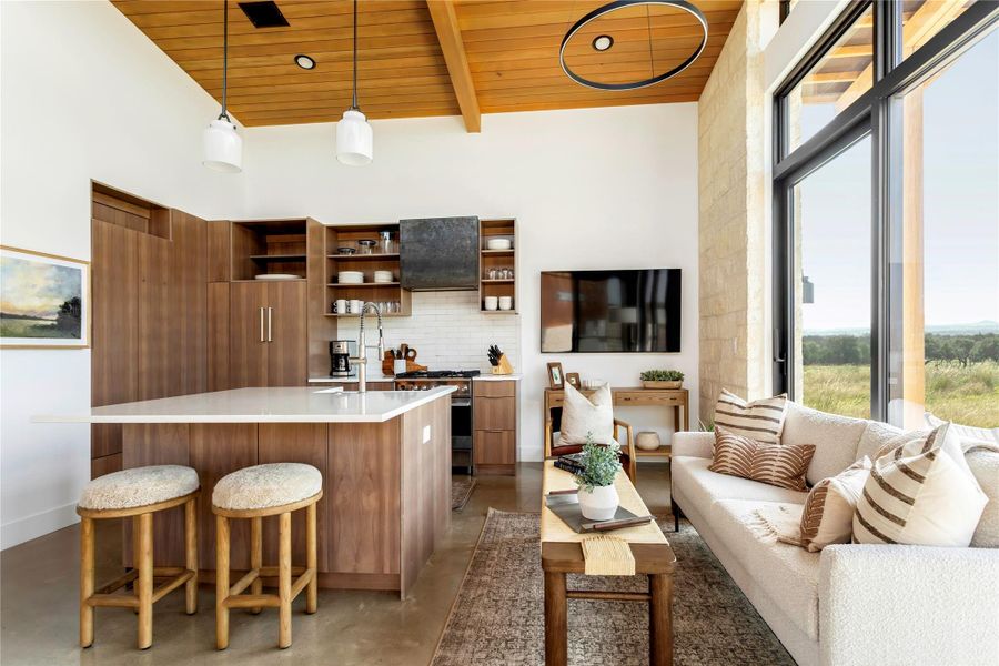 Bright open-concept living and kitchen area with soaring ceilings, custom cabinetry, and oversized windows framing scenic views. Bright open-concept living and kitchen area with soaring ceilings, custom cabinetry, and oversized windows framing scenic views.