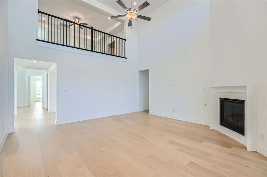 Unfurnished living room featuring high vaulted ceiling, light wood-style flooring, a ceiling fan, a glass covered fireplace, and baseboards