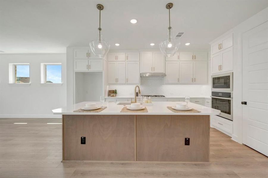 Contemporary kitchen featuring a light wood-finish island with a white countertop, two pendant lights, white cabinetry, integrated stainless steel appliances, and wood-finish flooring