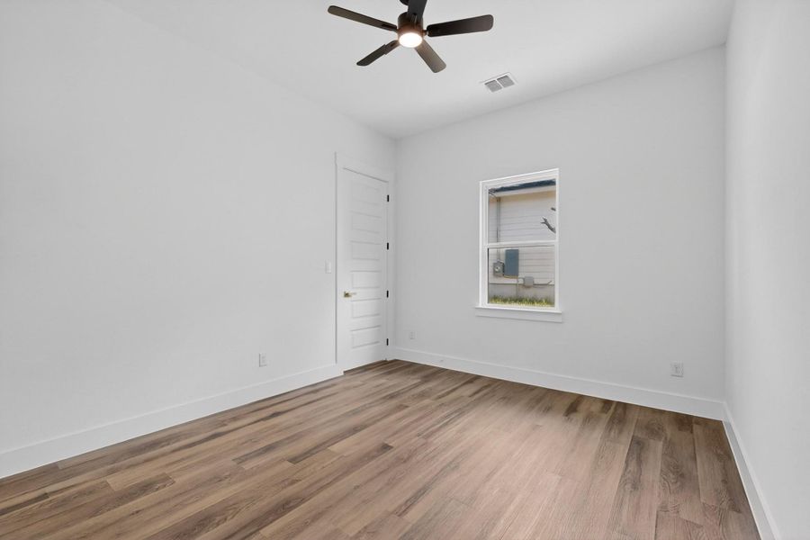 A well-lit room featuring durable hardwood flooring and a functional ceiling fan.