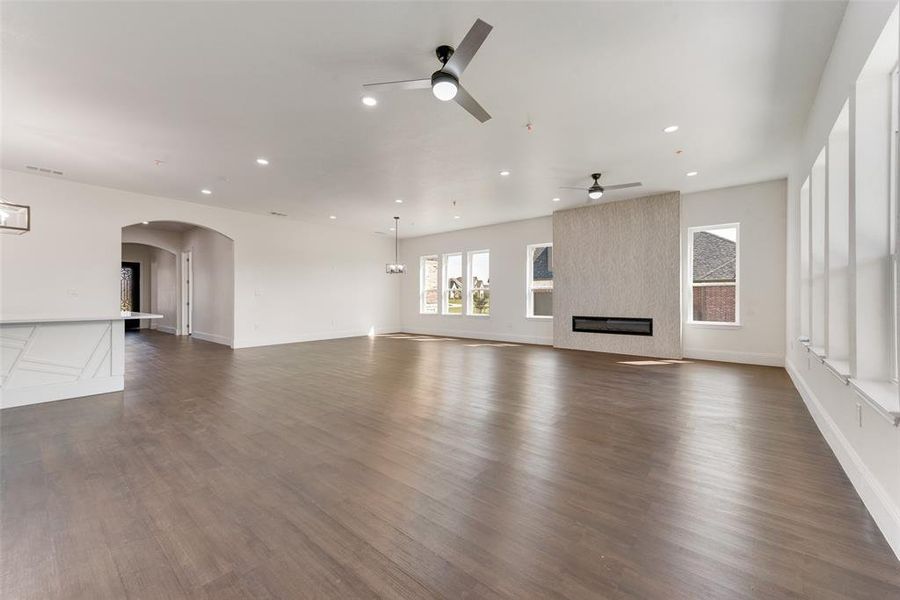 Expansive living area featuring wide plank wood-finish flooring, a modern fireplace with a textured surround, recessed lighting, and multiple ceiling fans Expansive living area featuring wide plank wood-finish flooring, a modern fireplace with a textured surround, recessed lighting, and multiple ceiling fans