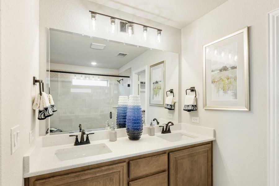 Bathroom with double sink vanity, wood cabinets, white countertop, and large mirror with overhead lighting