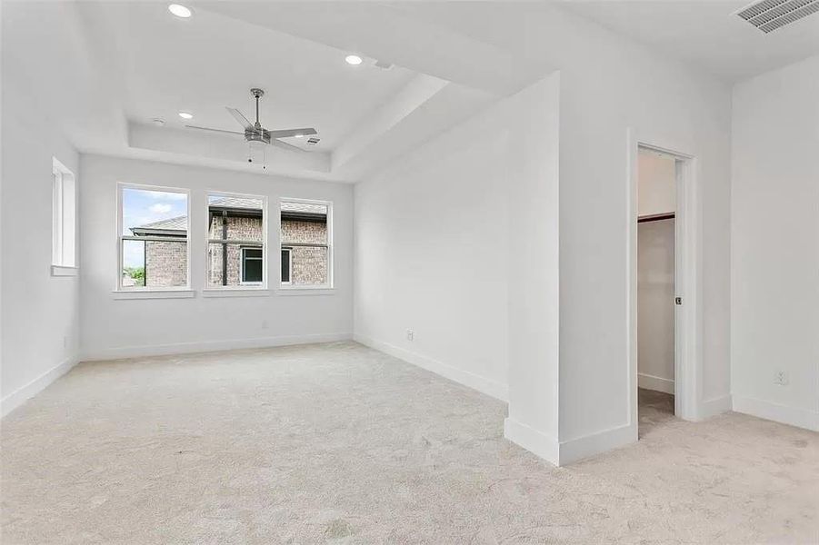 Carpeted spare room featuring a tray ceiling and ceiling fan