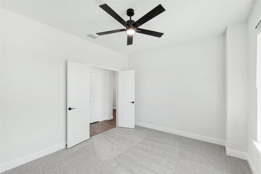Empty bedroom with gray carpet, black ceiling fan, and two white doors