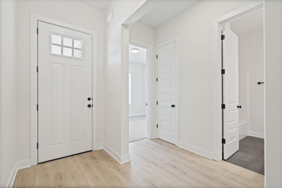 Entryway featuring a white paneled door with an upper window insert, matte black hardware, and wood-finish flooring Entryway featuring a white paneled door with an upper window insert, matte black hardware, and wood-finish flooring