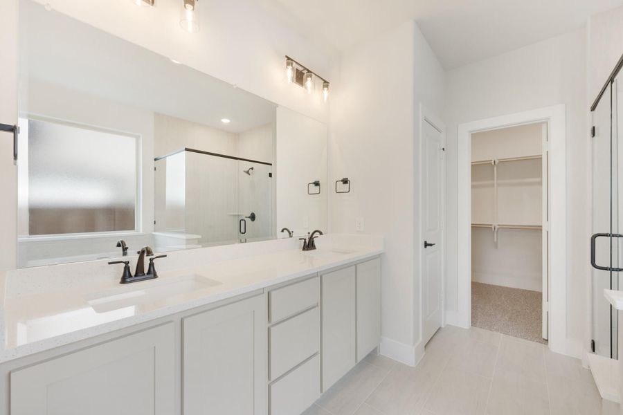 Master bathroom with double vanity, white quartz countertops, glass shower, and walk-in closet access
