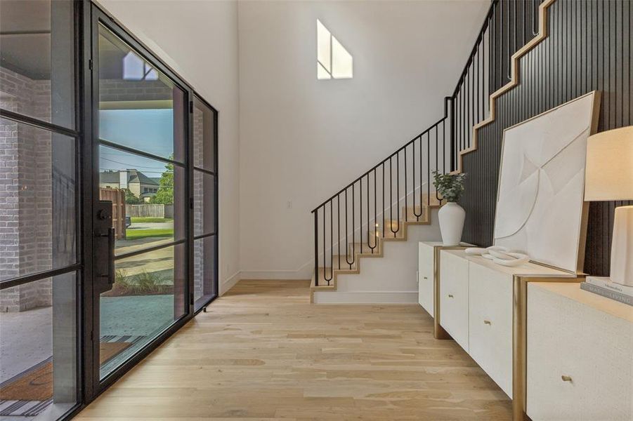 Entryway featuring a black metal and glass pivot door, light wood-finish flooring, a contemporary staircase with black metal balusters, and a black paneled accent wall Entryway featuring a black metal and glass pivot door, light wood-finish flooring, a contemporary staircase with black metal balusters, and a black paneled accent wall
