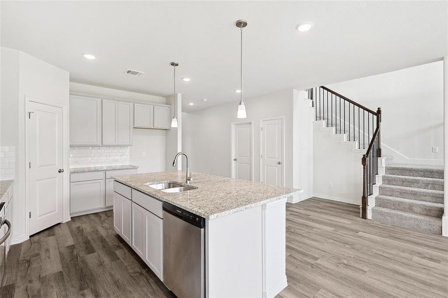 Kitchen with an island with sink, hardwood / wood-style flooring, stainless steel dishwasher, and backsplash