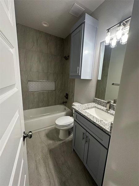 Full bathroom with tile flooring, oversized vanity, toilet, and tiled shower / bath combo