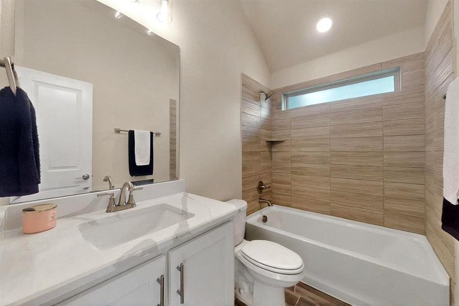 Bathroom with shower / tub combination, vaulted ceiling, toilet, and vanity