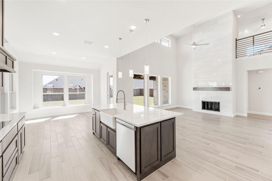 Open-concept kitchen with dark island, white countertops, and high ceilings flowing into living area with fireplace Open-concept kitchen with dark island, white countertops, and high ceilings flowing into living area with fireplace