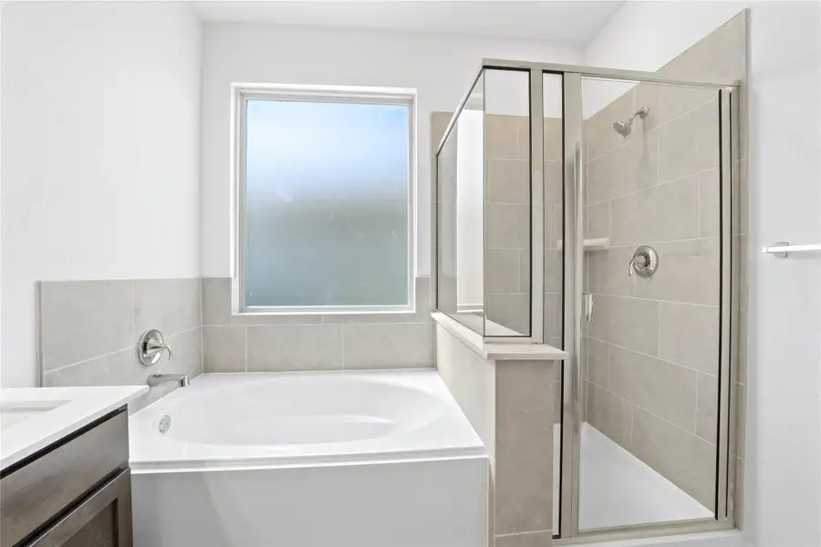 This additional view of the primary bath highlights a walk-in shower with elegant tile surround, a separate garden tub ideal for relaxing after a long day, and a large rain glass window that offers both natural light and privacy.