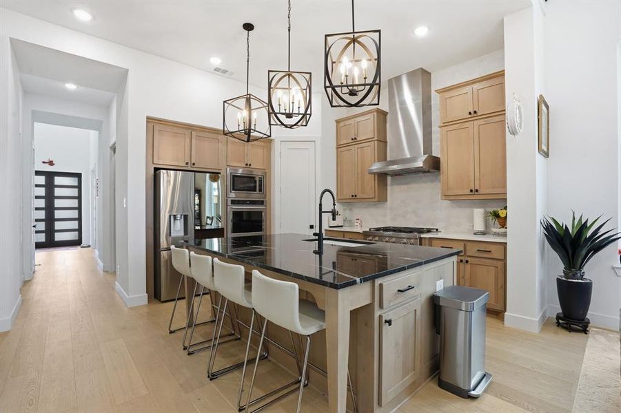 Kitchen featuring light brown cabinetry, backsplash, dark stone counters, light wood-type flooring, and stainless steel appliances Kitchen featuring light brown cabinetry, backsplash, dark stone counters, light wood-type flooring, and stainless steel appliances