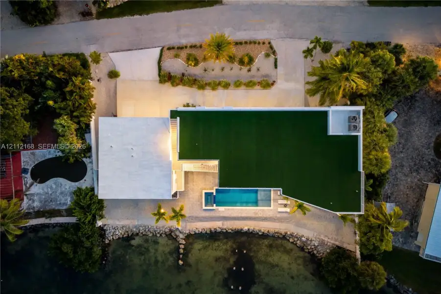 Aerial perspective featuring a waterfront property with an in-ground pool, concrete paved driveway, and established landscaping Aerial perspective featuring a waterfront property with an in-ground pool, concrete paved driveway, and established landscaping