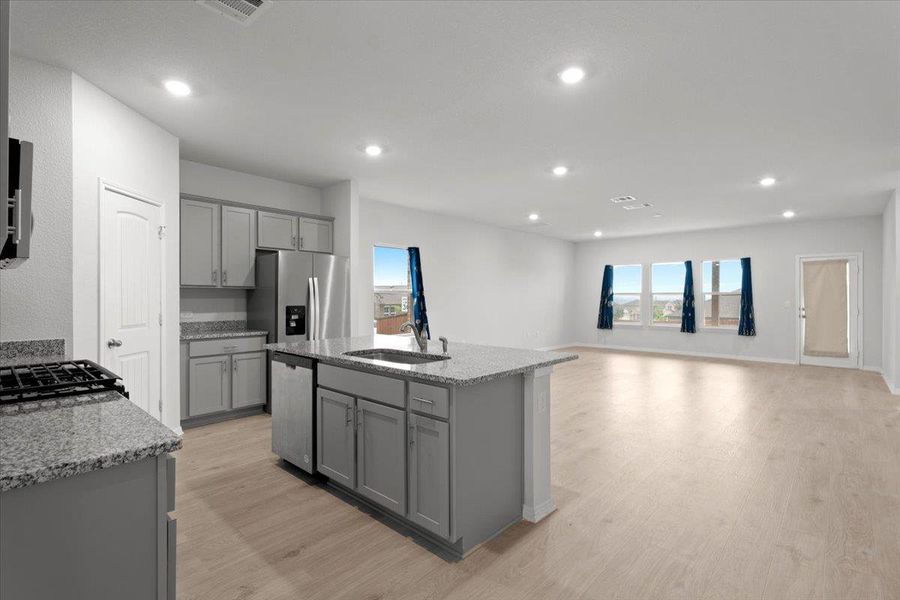 Open-concept kitchen and living area featuring granite countertops, stainless steel appliances, light wood-finish flooring, recessed lighting, and multiple windows