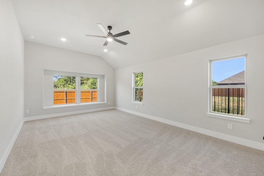 Empty bedroom with vaulted ceiling, ceiling fan, carpet flooring, and multiple windows