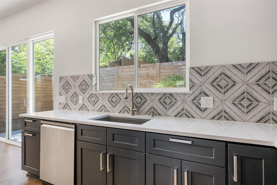 Kitchen featuring light stone countertops, stainless steel dishwasher, healthy amount of natural light, and decorative backsplash