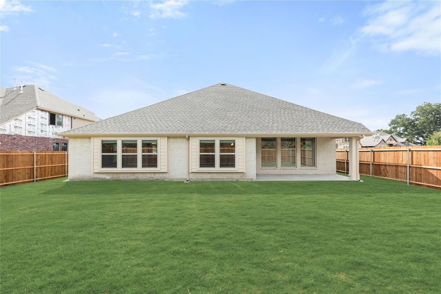 Rear exterior of single-story brick home with hip roof, patio, and fenced backyard with green lawn