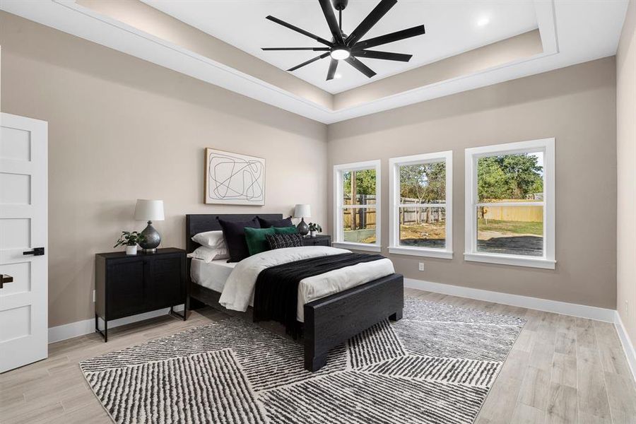 Bedroom featuring ceiling fan, light wood-type flooring, and a tray ceiling