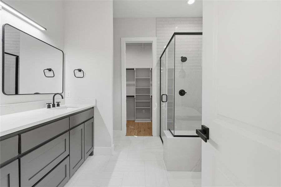 Bathroom featuring a vanity with quartz countertop, a black-framed mirror, and a glass-enclosed shower with subway tile surround Bathroom featuring a vanity with quartz countertop, a black-framed mirror, and a glass-enclosed shower with subway tile surround