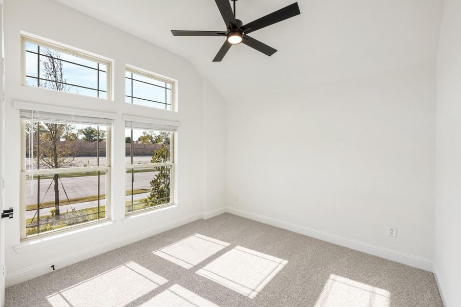 Empty bedroom with vaulted ceiling, ceiling fan, carpet flooring, and large windows with natural light Empty bedroom with vaulted ceiling, ceiling fan, carpet flooring, and large windows with natural light