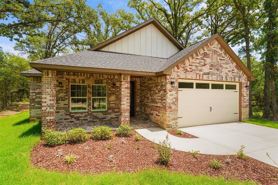 Brick and siding exterior featuring a covered front porch, an attached garage with decorative hardware, a concrete driveway, and established landscaping Brick and siding exterior featuring a covered front porch, an attached garage with decorative hardware, a concrete driveway, and established landscaping