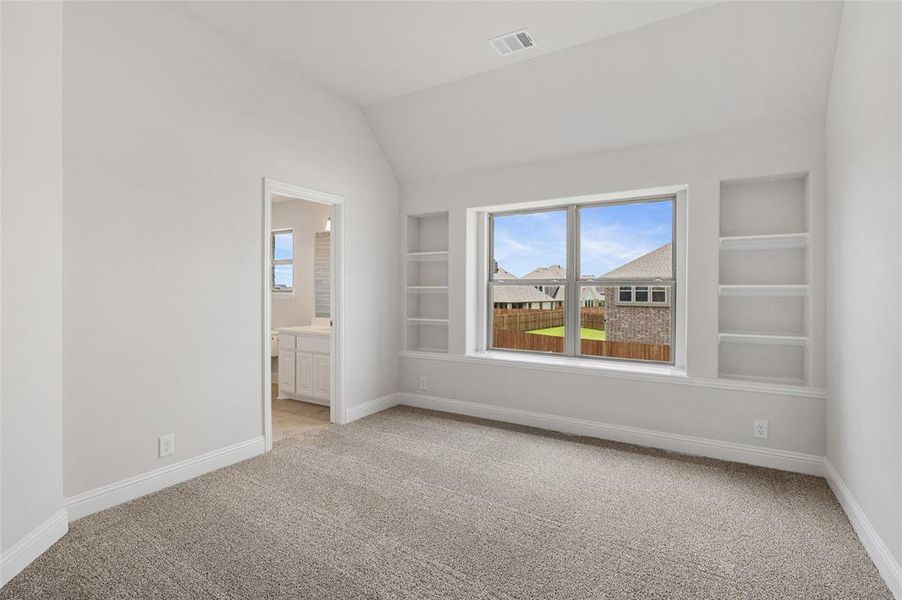 Empty room with built in shelves, light carpet, and lofted ceiling