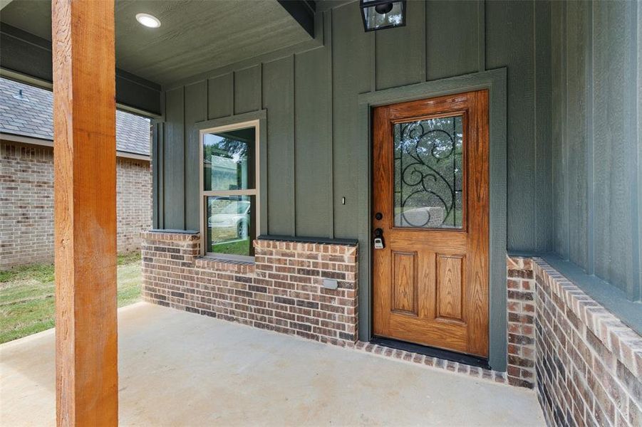 Doorway to property with board and batten siding, covered porch, and brick siding