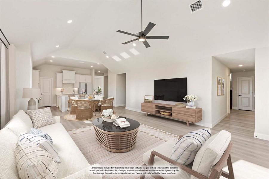 Open-concept living room with vaulted ceiling, ceiling fan, and light wood floors, open to dining area and white kitchen beyond.