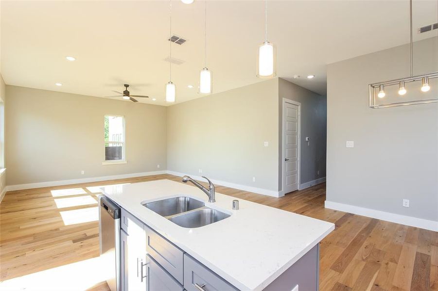 Kitchen featuring sink, light hardwood / wood-style flooring, a kitchen island with sink, decorative light fixtures, and stainless steel dishwasher