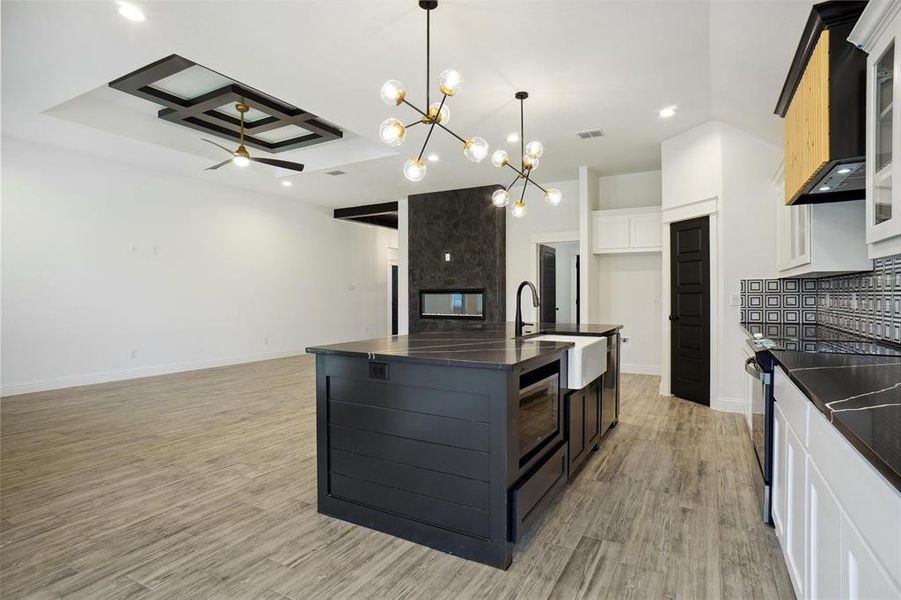 Kitchen with a center island with sink, sink, light hardwood / wood-style floors, ceiling fan with notable chandelier, and coffered ceiling