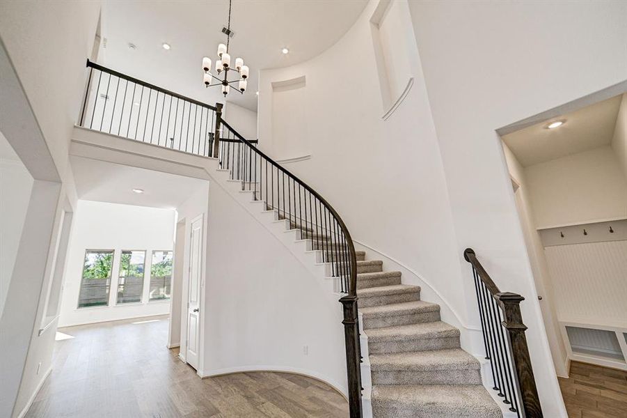 Grand stairwell features wood and iron railing. (note: upgraded mud bench added to the right by garage entry)