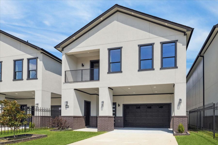 The front elevation stands out with a fresh contemporary profile, defined by smooth stucco, deep-toned accents, and a second-story balcony that adds depth and dimension.