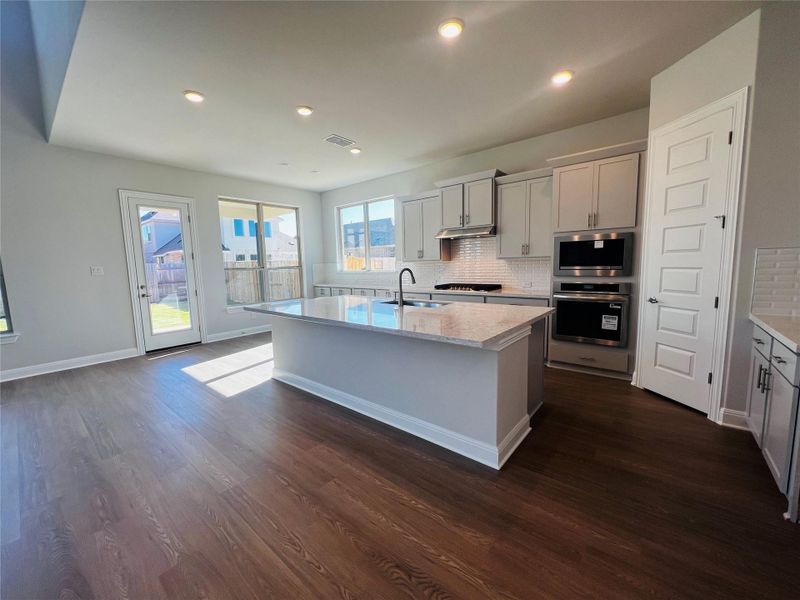 Kitchen featuring backsplash, appliances with stainless steel finishes, a kitchen island with sink, light stone countertops, and recessed lighting