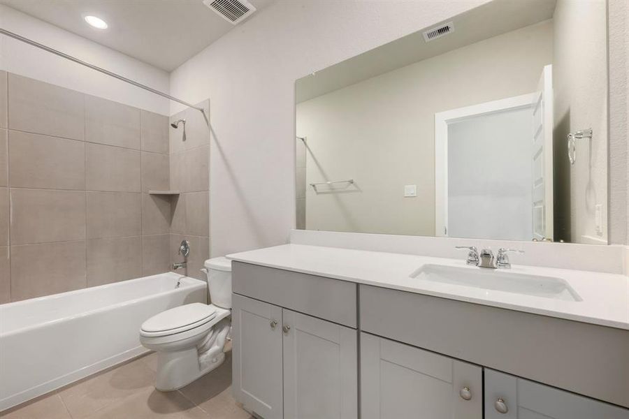 Secondary bathroom features light countertops and grey cabinets, neutral paint, shower/tub combo with tile surround, large mirror, tile floors, sleek fixtures and modern finishes, plenty of space to accommodate any visiting family or guests.