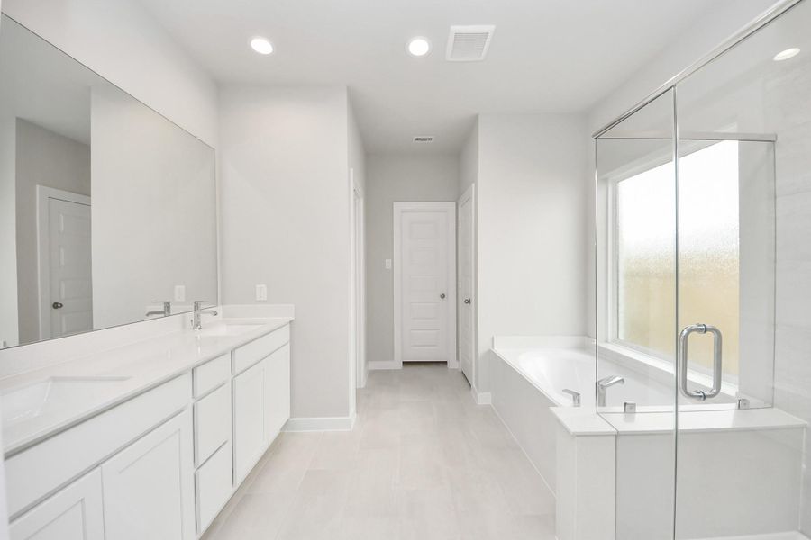 Escape to a spa-like oasis in this primary bathroom. Enjoy a walk-in shower with tile surround, a separate garden tub with custom detailing, and an elegant vanity featuring light countertops, modern hardware, and beautiful recessed lights. Experience luxury and relaxation in every detail. Sample photo of completed home with similar floor plan. Actual colors and selections may vary.