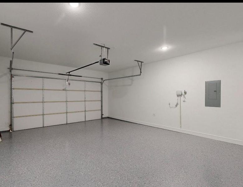 Garage with electric panel, baseboards, and a garage door opener