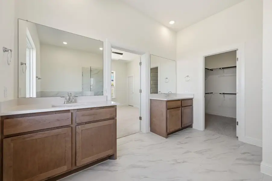 Bathroom with a spacious closet, light marble finish floors, two vanities, and recessed lighting