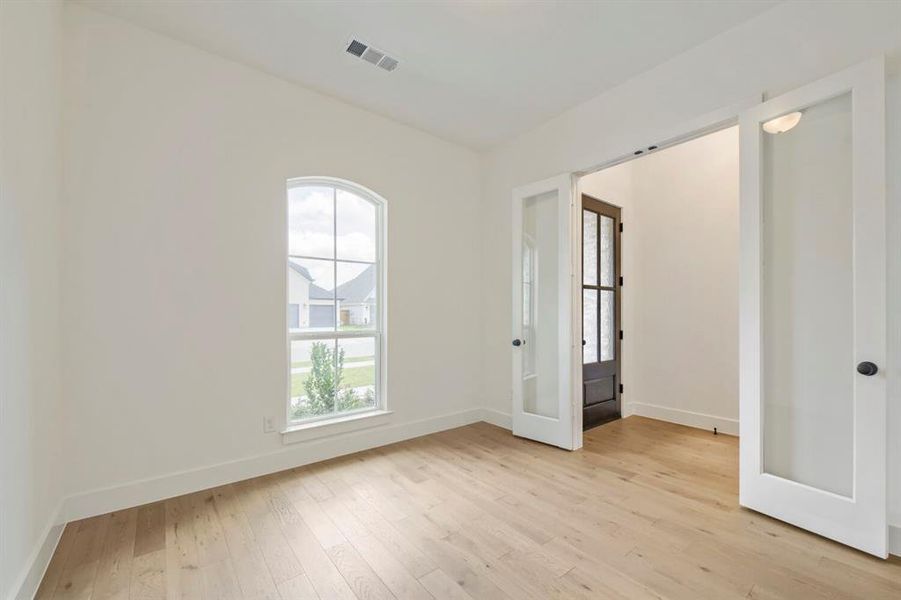 Spacious room featuring light wood-finish flooring and a white arched window Spacious room featuring light wood-finish flooring and a white arched window