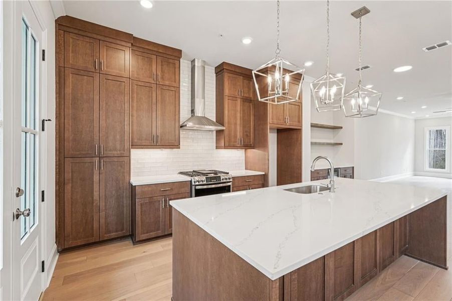 Kitchen featuring light stone counters, light wood-style flooring, gas stove, an island with sink, and tasteful backsplash