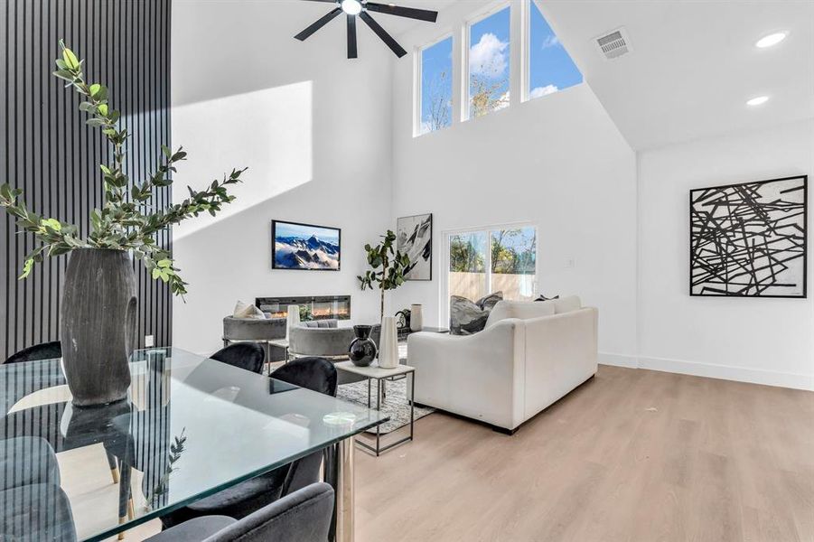 Living room with ceiling fan, a high ceiling, and light wood-type flooring