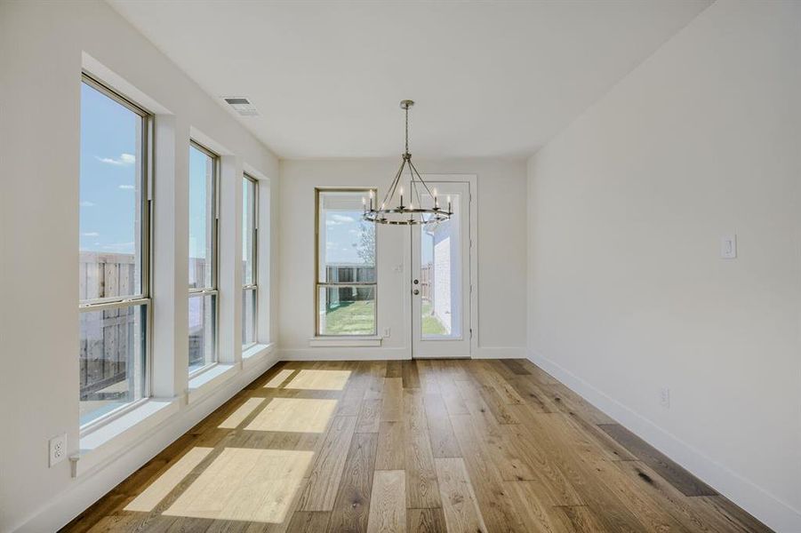 Open concept room featuring wood-finish flooring, a contemporary chandelier, multiple large windows, and a glass-paneled door