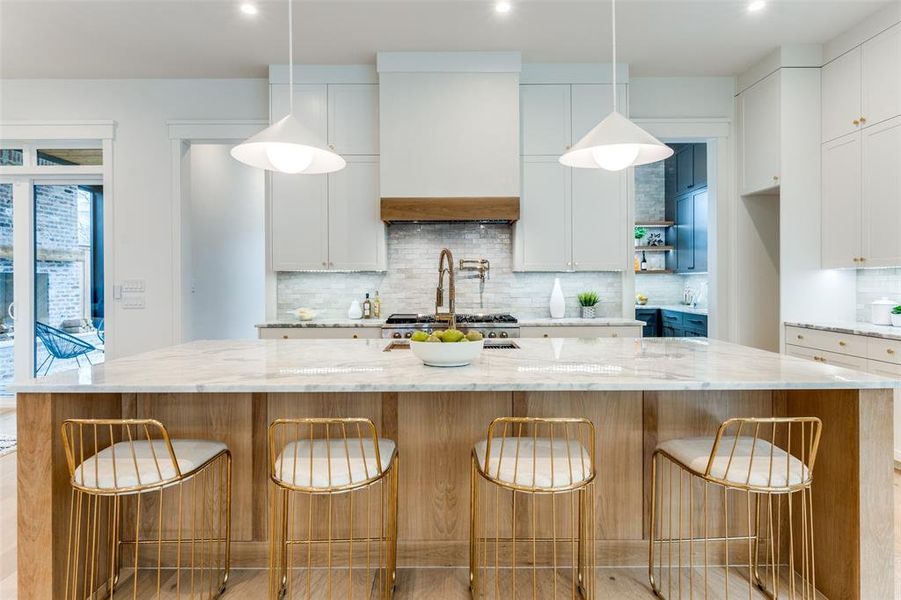 Kitchen with pendant lighting, a spacious island, light stone countertops, and white cabinets