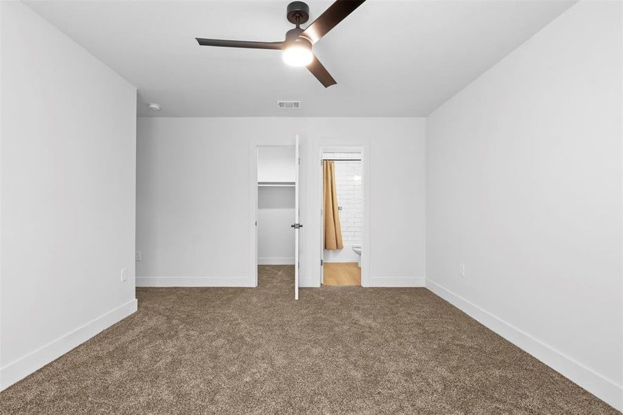 Unfurnished bedroom featuring carpet flooring, ceiling fan, a closet, a walk in closet, and ensuite bath