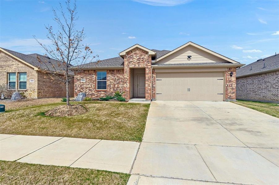 Ranch-style house featuring a front yard, concrete driveway, brick siding, a shingled roof, and a garage
