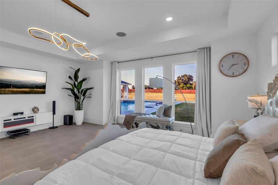 Primary Bedroom:A grand retreat where scale meets serenity, the primary bedroom is framed by expansive windows that capture views of the pool and grounds beyond. Elevated by designer lighting and space for both rest and relaxation, it offers a private sanctuary of elegance and effortless luxury.